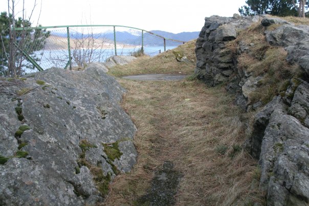 Løpegrav delvis nedsprengt i berget fører inn til restene etter en av luftvernstillingene på Storhaugen.