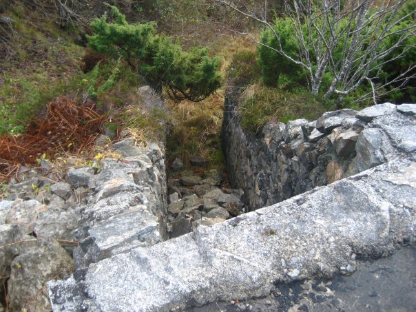 Løpegrav som er delvis gjenfylt fører fra bunkeren og ned til den første av de fire 10,5cm stillingene.